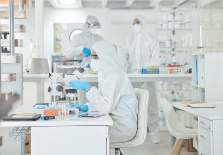 Executing laboratory testing according to standard procedures. a scientist wearing a radiation suit while using a microscope in a lab.の写真素材