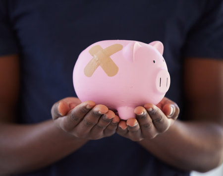 Its never too late to pay off your debt. an unrecognisable man holding a piggybank with a band aid over it.の写真素材