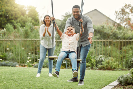 Family is the most important thing in the world. parents playing with their son on the swing outside.の写真素材