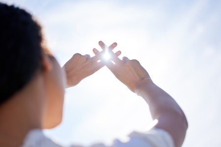 Praise the sun gods. Low angle shot of a woman holding her hands up to a sunny sky and making hand gestures.の写真素材