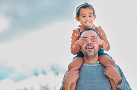 He doesnt know that its me. a little girl covering her fathers eyes while sitting on his shoulders outdoors.の写真素材