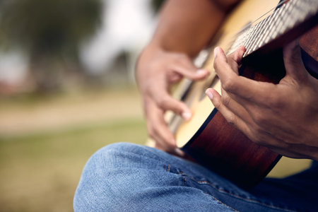 Make life a song wherever you are. an unrecognisable man playing the guitar outside at college.