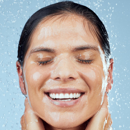 Fresh is best. Studio shot of an attractive young woman taking a shower against a blue background.の写真素材