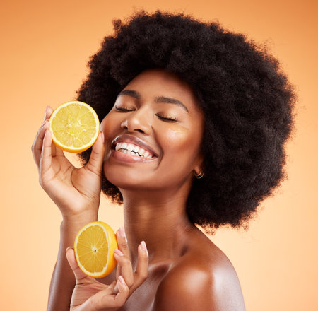 Beauty, skincare and orange with a model black woman in studio on a color wall background. Skin, health and vitamin c with a young female holding fruit for wellness, nutrition or natural treatmentの写真素材