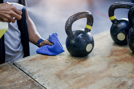 Performing regular cleaning and maintenance of gym equipment. Closeup shot of an unrecognisable man sanitising a kettlebell while working in a gym.の写真素材