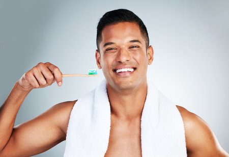 Mouth, dental and man brushing teeth in studio for hygiene, wellness and grooming against a grey background. Portrait, teeth and oral care by happy guy enjoying fresh, clean and toothpaste routineの写真素材