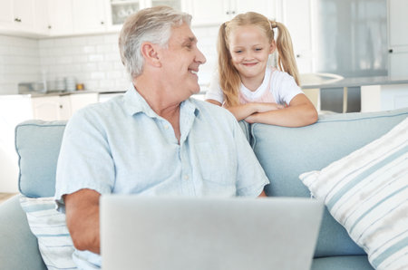 Laptop, elearning and senior family with child for online education, kids website communication and internet teaching at home on sofa. Grandfather and girl with technology play internet game togetherの写真素材