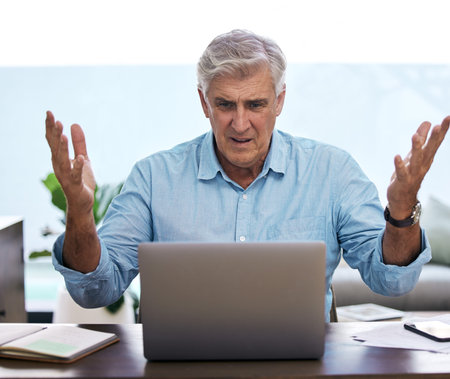 What is this laptop doing. a mature man sitting alone and feeling frustrated while using his laptop...