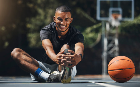 Training, basketball player and man stretching legs in outdoor community court, muscle energy and healthy sports game performance. Happy, strong and young male athlete warm up exercise in competitionの写真素材