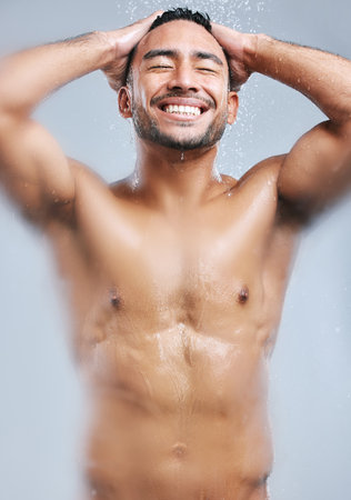 A warm shower always wakes me up. Studio shot of a handsome young man taking a shower against a grey background.の写真素材