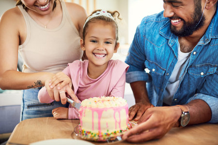 A birthday girl has to cut her cake. a little girl celebrating a birthday with her parents at home.の写真素材