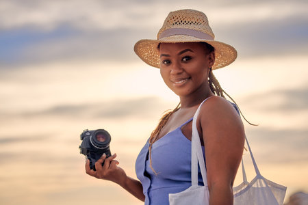 Navigating muddy waters. Portrait of a young beautiful woman taking pictures with her camera at sunset at the beach.の写真素材
