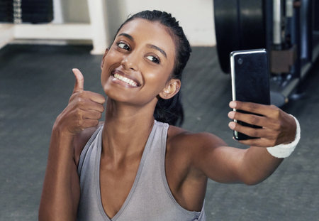 A little progress each day will lead to great results. a sporty young woman showing thumbs up while taking selfies in a gym.の写真素材