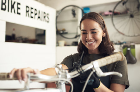 You are ready for a new owner. an attractive young woman standing alone in her shop and repairing a bicycle.の写真素材