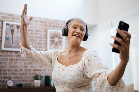 The fountain of youth is filled with lots of fun. a senior woman dancing while using a smartphone and headphones at home.の写真素材