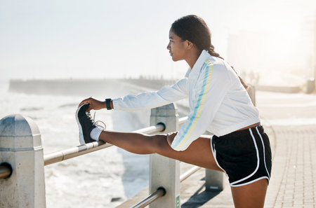 Stretching legs, fitness and woman training in nature for motivation in morning, health and outdoor run. Strong, thinking and young athlete runner doing warm up before running by the ocean for cardioの写真素材