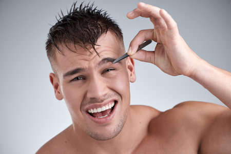 Setting my own standards. Closeup portrait of a young handsome man tweezing his eyebrows against a grey background.の写真素材