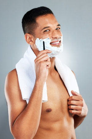 Man shaving face, razor and shower for hair removal, aesthetic skincare and facial cleaning on grey studio background. Portrait happy naked guy, shave foam and body cream cosmetics for wellnessの写真素材