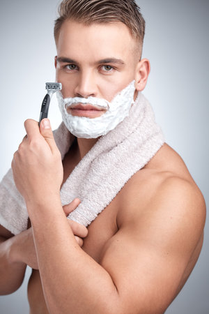 A strand for every heart Ill break. Studio portrait of an attractive young man shaving his face against a grey background.の写真素材