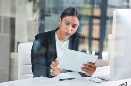 Whats going on here. an attractive young businesswoman sitting alone in her office and using a digital tablet.の写真素材