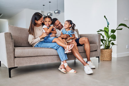 Family, children and laugh with a girl, sister and parents sitting on a sofa in the home living room together. Kids, laugh and humor with a mother, father and daughter siblings bonding in a houseの写真素材