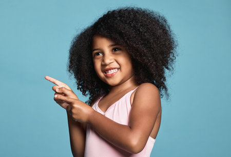 .Advertising, hand and child with smile, happy and finger for blue mockup studio background. Face of a young African girl in happiness while pointing to show attention to marketing and mock up space.の写真素材