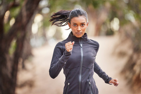 Getting in my daily cardio. a young woman jogging through a forest.