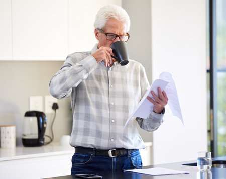 A cup of tea makes all the difference. a mature man reading paperwork while drinking tea.の写真素材