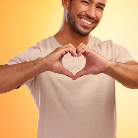 My heart beats for you. a man forming a heart shape with his hands while standing against a yellow background.の写真素材