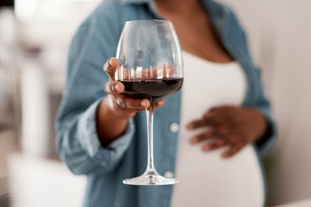 Alcohol can harm the developing baby while pregnant. Closeup shot of a pregnant woman holding a glass of red wine at home.の写真素材
