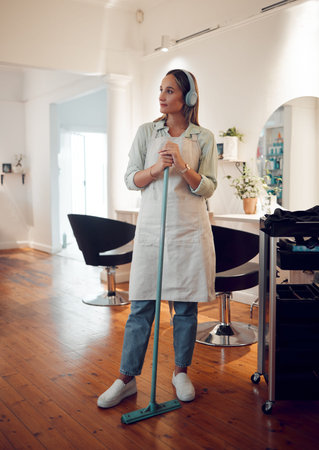 Salon, headphones and woman cleaner sweeping her workplace while listening to music, radio or...