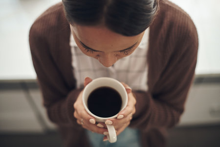 Enjoying a dark and soothing cup. High angle shot of a young woman drinking coffee at home.の写真素材