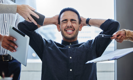 Im gonna scream. a young businessman sitting in the office and feeling stressed while colleagues overwhelm him with tasks.の写真素材
