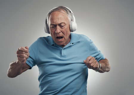 What a funky tune. an elderly male wearing headphones and listening to music in a studio against a grey background.の写真素材