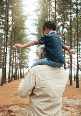 Grandfather, child and shoulders for walk in forest, nature or woods together for bonding. Senior, man and kid with trees, sunshine and walking for playing, fun and happiness on vacation with familyの写真素材