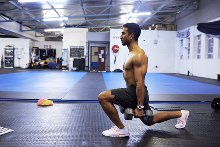Building those thigh muscles. a young man using weights while doing lunges in the gym.の写真素材