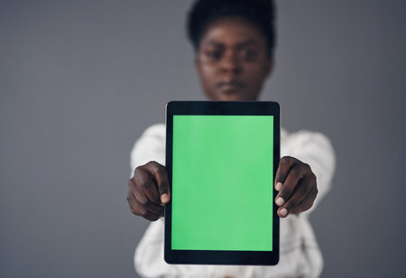 I designed the perfect website for you. an attractive young businesswoman standing against a grey background in the office and holding a digital tablet.の写真素材