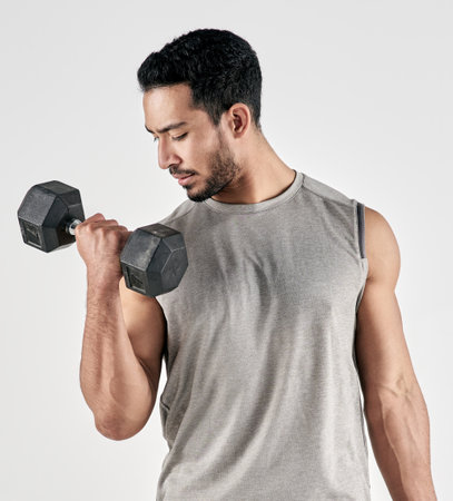 Lifting heavy and making gains. Studio shot of a muscular young man exercising with a dumbbell against a white background.の写真素材