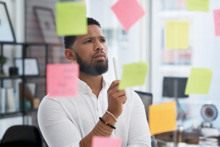 Somethings missing... I just have to figure it out. a young businessman brainstorming with sticky notes on a glass wall in an office.の写真素材