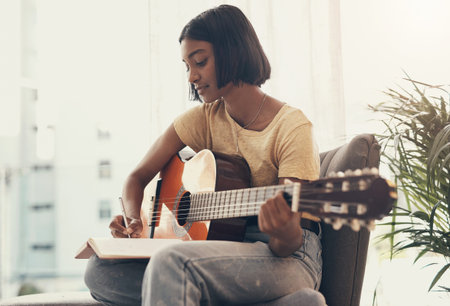 Surrounded yourself with inspirational people, starting with you. a young woman playing the guitar at home.の写真素材