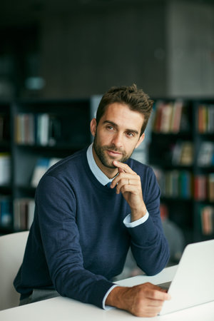 Go on, Im listening. a handsome young businessman sitting in a library and looking contemplative...