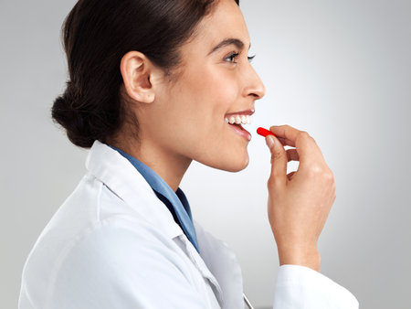 Take one pill and call myself in the morning. Studio shot of a young doctor taking medication against a grey background.の写真素材