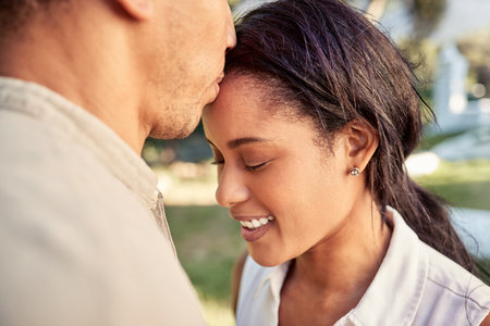 Couple, love and outdoor park for bonding with a kiss on forehead showing commitment, trust and support with a smile. Happiness, care and nature with a young man and woman in a romantic relationshipの写真素材