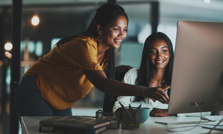 Success is something to pursue through hard work. two young businesswomen working together on a computer in an office at night.の写真素材