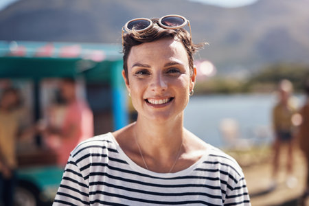 Why stay at home when you can go outside. Portrait of a cheerful young woman smiling brightly while standing outside on a beach promenade during the day.の写真素材