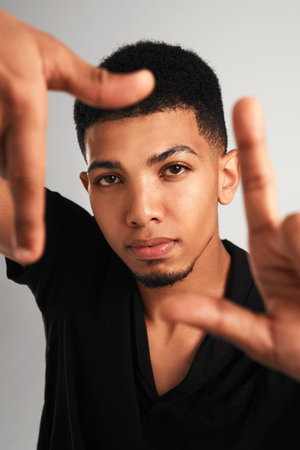 Frame by frame. Portrait of a handsome young man making a frame with his fingers while standing against a grey background inside of a studio.の写真素材