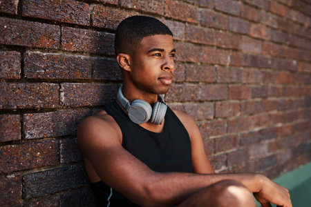 Just me and my dreams today. a sporty young man sitting against a wall outdoors.