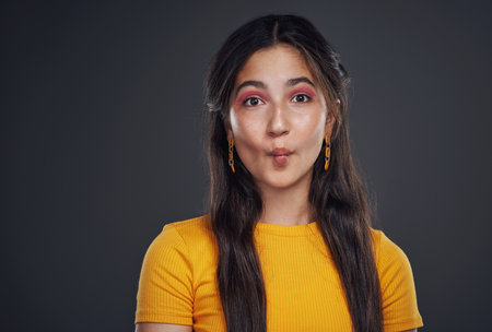 Funny faces are my thing. Cropped portrait of an attractive teenage girl standing alone and feeling playful against a dark background in the studio.の写真素材