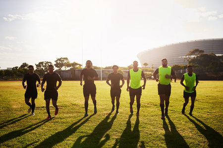 We run every day. Full length shot of a diverse group of sportsmen warming up before playing rugby during the day.の写真素材