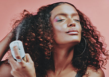 Put a hold on it. a young woman spraying hairspray on her curly hair.の写真素材